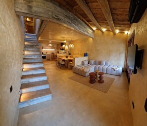 Ein großzügiger Innenraum mit einer Treppe, die zu einer Küchenzeile führt, einem Sitzbereich mit Sofa und Couchtisch sowie einem an der Wand montierten Fernseher.