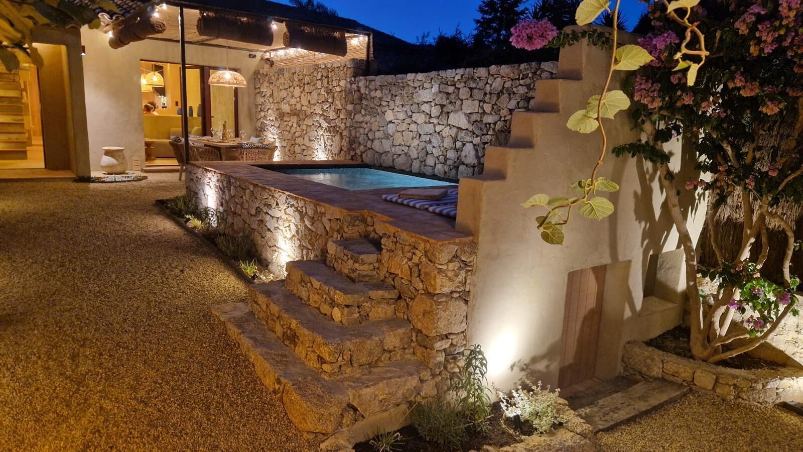 A stone staircase leading to a pool area, surrounded by a stone wall and a thatched roof structure.