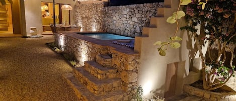 A stone staircase leading to a pool area, surrounded by a stone wall and a thatched roof structure.