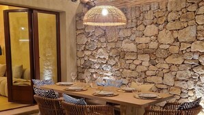 A dining area with a stone wall, a wooden table, wicker chairs, and a hanging light fixture. - Casa Solea - Gulf of Saint-Tropez (Le Plan-de-la-Tour)