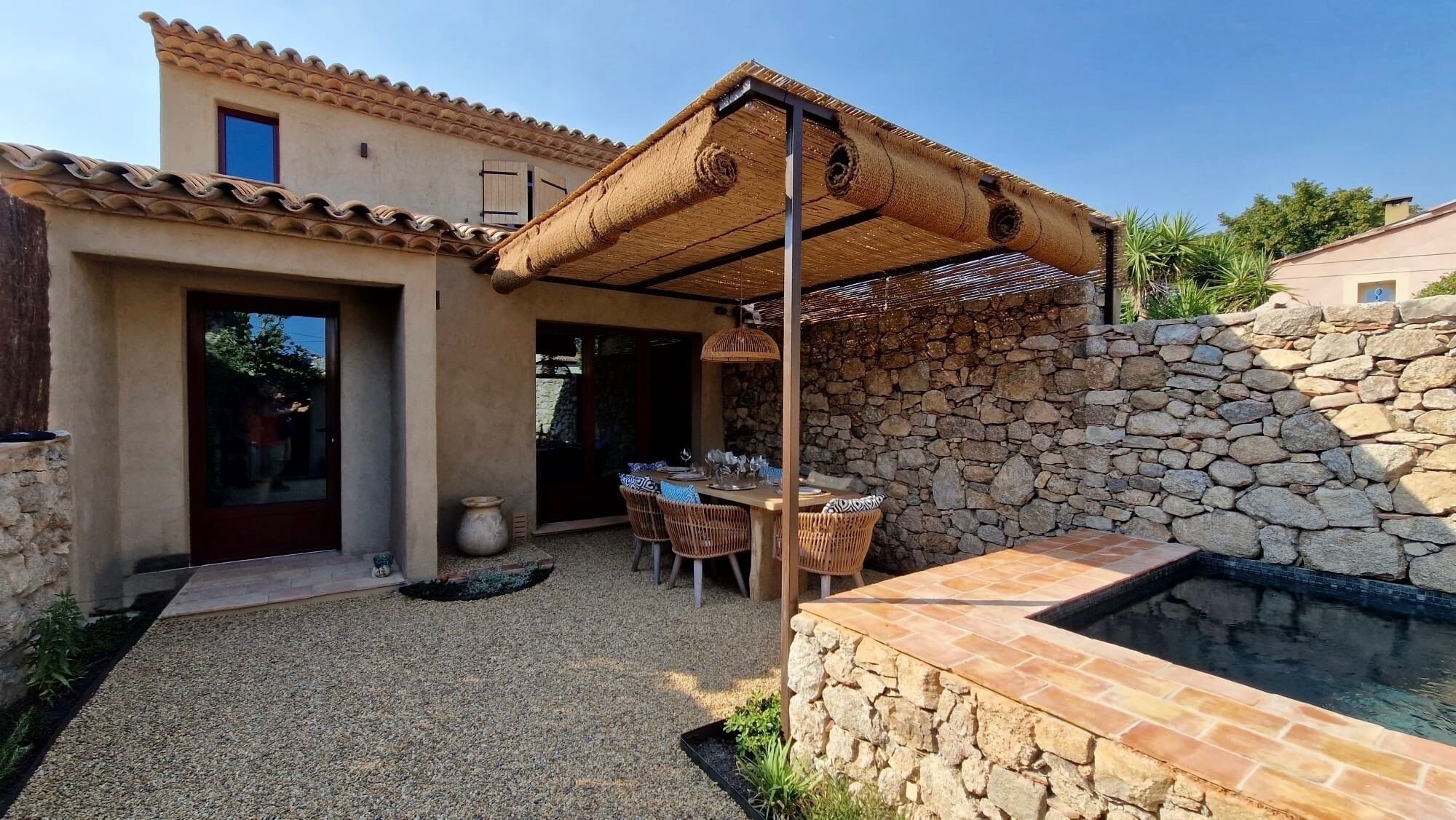Eine Terrasse mit Steinmauer, Tisch und Stühlen sowie einem Reetdachbau.