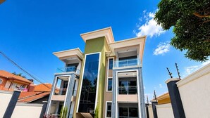 A modern multi-story building with a central glass facade, surrounded by a paved courtyard with plants. - Uptown Homes Kampala (Kampala)