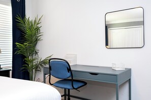 A hotel room with a bed, a desk, a chair, a potted plant, a mirror, and a white bedside table. - ☆☆☆☆☆Price Drop! OCT-NOV - 4BR ChampionsGate - Pool - Themed Rooms! 
☆☆☆☆☆ (Davenport)