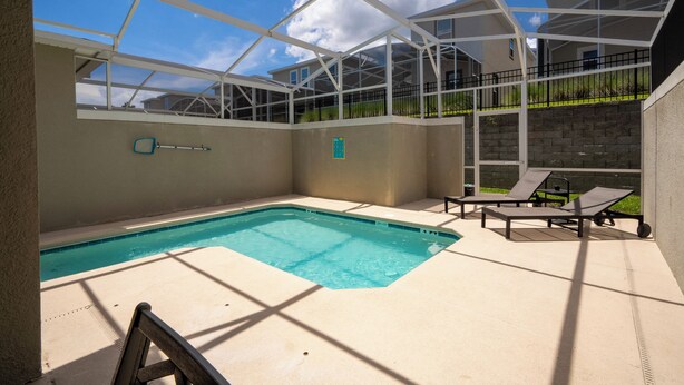 A swimming pool with a glass enclosure, lounge chairs, and a view of a residential area. - Relaxing 4BR ChampionsGate Getaway - Private Pool, BBQ & Family Comfort (Davenport)