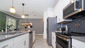 A modern kitchen with stainless steel appliances, a grey tiled backsplash, and pendant lighting. - Relaxing 4BR ChampionsGate Getaway - Private Pool, BBQ & Family Comfort (Davenport)