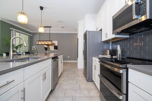 A modern kitchen with stainless steel appliances, a grey tiled backsplash, and pendant lighting. - Relaxing 4BR ChampionsGate Getaway - Private Pool, BBQ & Family Comfort (Davenport)