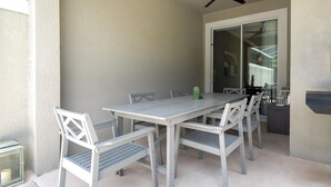 A covered patio with a table and chairs, a ceiling fan, and a sliding glass door leading to an interior space. - Relaxing 4BR ChampionsGate Getaway - Private Pool, BBQ & Family Comfort (Davenport)