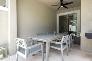 A covered patio with a table and chairs, a ceiling fan, and a sliding glass door leading to an interior space. - Relaxing 4BR ChampionsGate Getaway - Private Pool, BBQ & Family Comfort (Davenport)