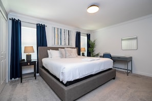 A modern bedroom with a large bed, bedside lamps, a desk, and a potted plant. - Relaxing 4BR ChampionsGate Getaway - Private Pool, BBQ & Family Comfort (Davenport)