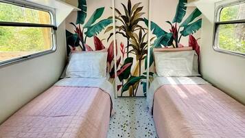 Una habitación pequeña y acogedora con dos camas, un ventanal y un mural en la pared.