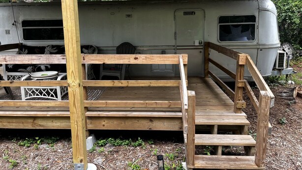 Una terraza de madera que conduce a un espacio cubierto, con una caravana estacionada al fondo.