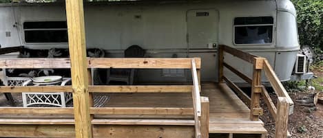 A wooden deck leading to a covered area with a camper parked in the background.