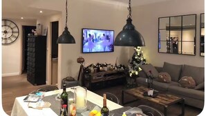 Ein Wohnzimmer mit Fernseher, einer Couch und einem Essbereich mit Tisch für zwei Personen.