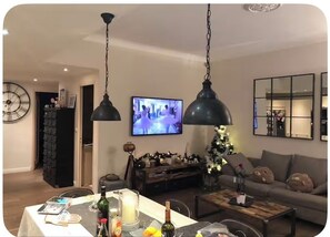 Ein Wohnzimmer mit Fernseher, einer Couch und einem Essbereich mit Tisch für zwei Personen.