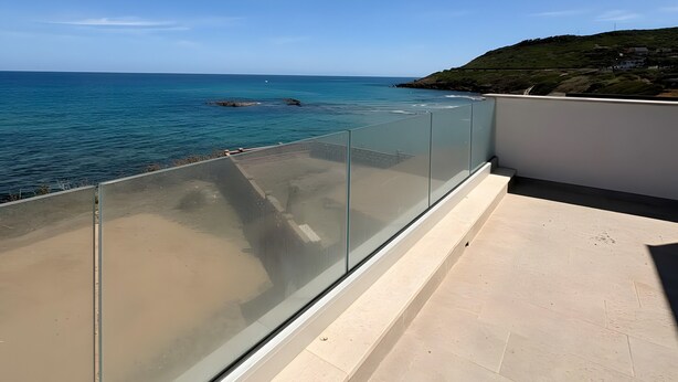 Een balkon met glazen hekwerk, met uitzicht op de kust.