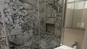 Een badkamer met een douchecabine van glas, voorzien van een bloemendesign, een wit wastafelmeubel en een spiegel.