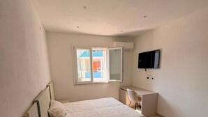 Een slaapkamer met een bed, bureau, stoel, televisie en raam.