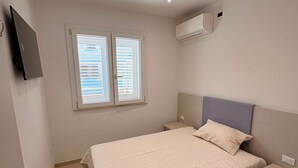Een slaapkamer met een bed, nachtkastje, televisie aan de muur en een airconditioner.