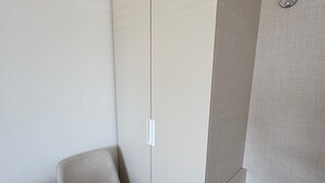 Een moderne kamer met een hoekbed, een stoel en een kledingkast.