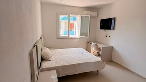 Ein Schlafzimmer mit Bett, Schreibtisch, Stuhl, Fernseher und Fenster.