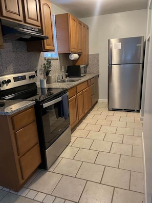 A kitchen with wooden cabinets, stainless steel appliances, and a tiled floor. - Cozy Beach Hideaway - 1 block to the beach (Jacksonville Beach)