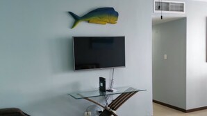 Uma sala de estar com televisão de tela plana na parede, um ventilador de teto e uma decoração com peixe.