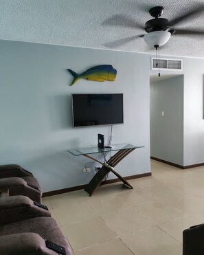 Ein Wohnzimmer mit einem an der Wand befestigten Flachbildfernseher, einem Deckenventilator und einer Fischdekoration.