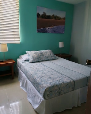 A bedroom with a bed, two bedside tables, a window with blinds, and a wall-mounted picture. - Luxury 3BR Jaco Retreat • Pool • Beach • Concierge Included (Jacó)