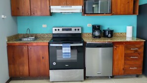 Uma cozinha com armários de madeira, micro-ondas, fogão, cafeteira e máquina de lavar louça.