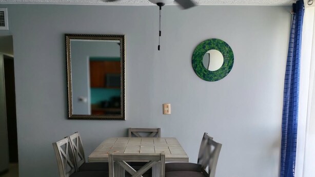 Uma área de refeições com mesa e cadeiras, um ventilador de teto, um espelho e um prato decorativo na parede.