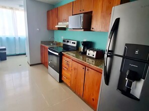 A kitchen with wooden cabinets, a stainless steel refrigerator, a microwave, a stove, and a coffee maker. - Luxury 3BR Jaco Retreat • Pool • Beach • Concierge Included (Jacó)