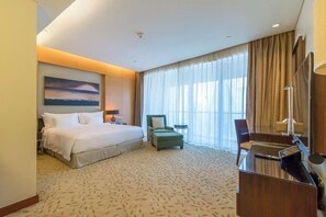A hotel room with a bed, a desk, a chair, a small table, and a large window with curtains. - Spacious Studio Fashion Ave Dubai Mall Burj view (Dubai)