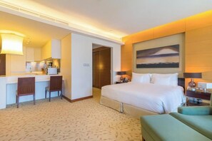 A hotel room with a bed, a desk with chairs, a painting on the wall, and a carpeted floor. - Spacious Studio Fashion Ave Dubai Mall Burj view (Dubai)