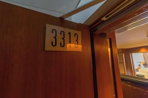 A hotel room number sign, a wooden door, and a glimpse of a room with a bed and a person. - Spacious Studio Fashion Ave Dubai Mall Burj view (Dubai)