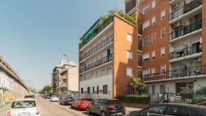 A multi-story residential building with balconies, parked cars, and a graffiti-covered wall. - Spacious apartment of approximately 100 sqm, accommodating up to 7 people, located on the fifth and top floor of a building with an elevator (NOT accessible to people with disabilities).The property is situated in the Cimiano district, just a 5-minute wa (Milan)