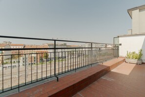 Ein Balkon mit Metallgeländer, der auf Gleise und Gebäude blickt.