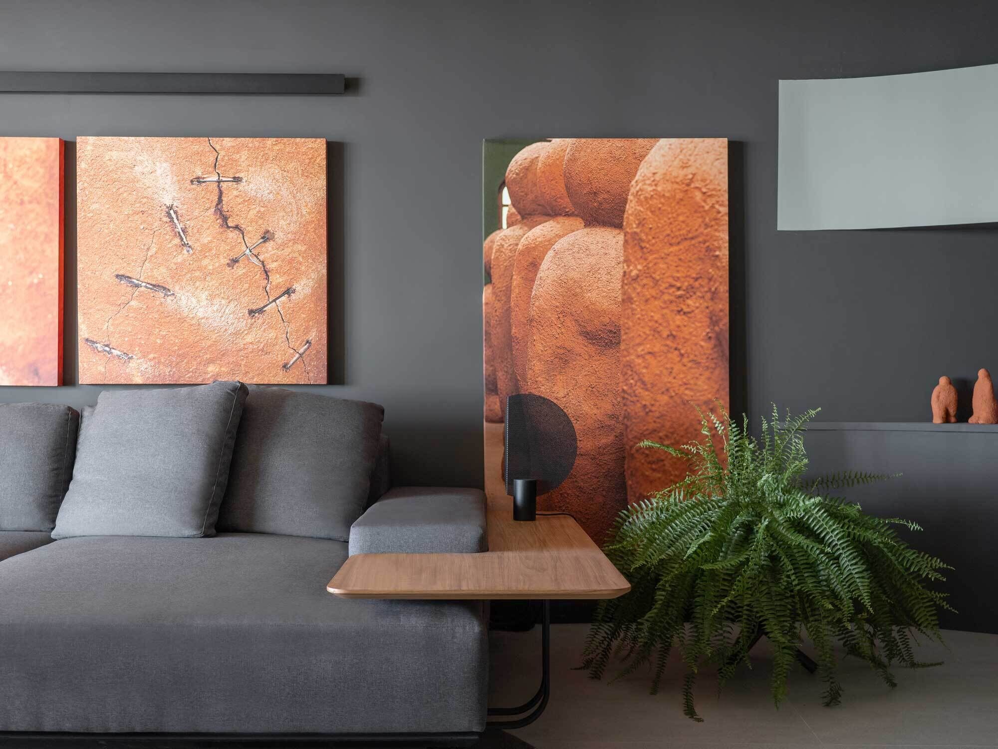 Una sala de estar moderna con un sofá gris, una mesita de madera, un cuadro abstracto grande, una planta de helecho y un altavoz.