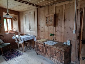 A rustic wooden room with a dining table, chairs, a bench, a patterned rug, and a wall-mounted radio. - Cozy historic Engadin-style house with Swiss stone pine (Ardez)