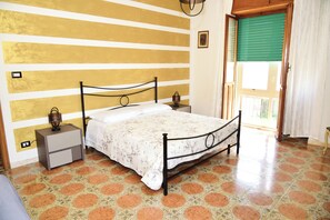 A bedroom with a bed, nightstands, a wall with horizontal stripes, a window with blinds, and a patterned floor. - Cozy apartment near the Temo (Bosa)
