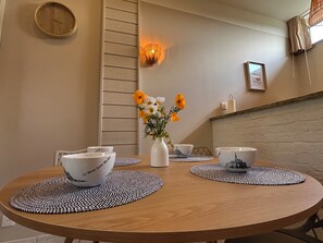 A round wooden table with placemats, white bowls, and a vase with flowers. - La Parenthèse de la Baie - Charme & nature près du Mont Saint Michel (Aucey-la-Plaine)