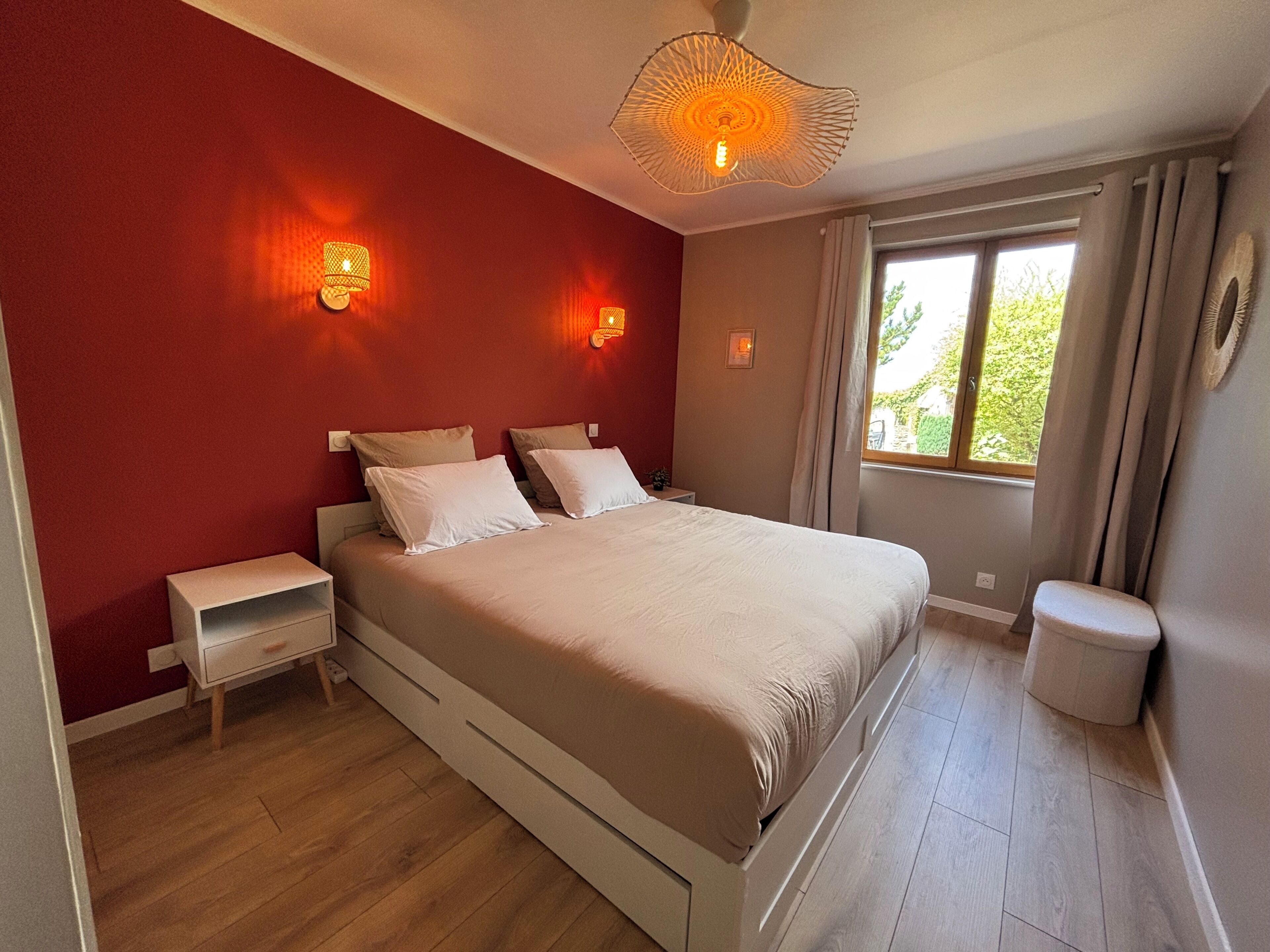 Un dormitorio con cama, mesitas de noche, una ventana con cortinas y un aplique de pared.