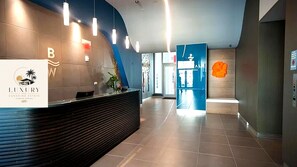 A reception area with a modern design, featuring a reception desk, a logo, and a blue wall with a geometric pattern. -  3BDR/3BA LUXURY OCEAN & SUNSET VIEW - Beach, Cruises, and Miami Minutes Away (Hallandale Beach)