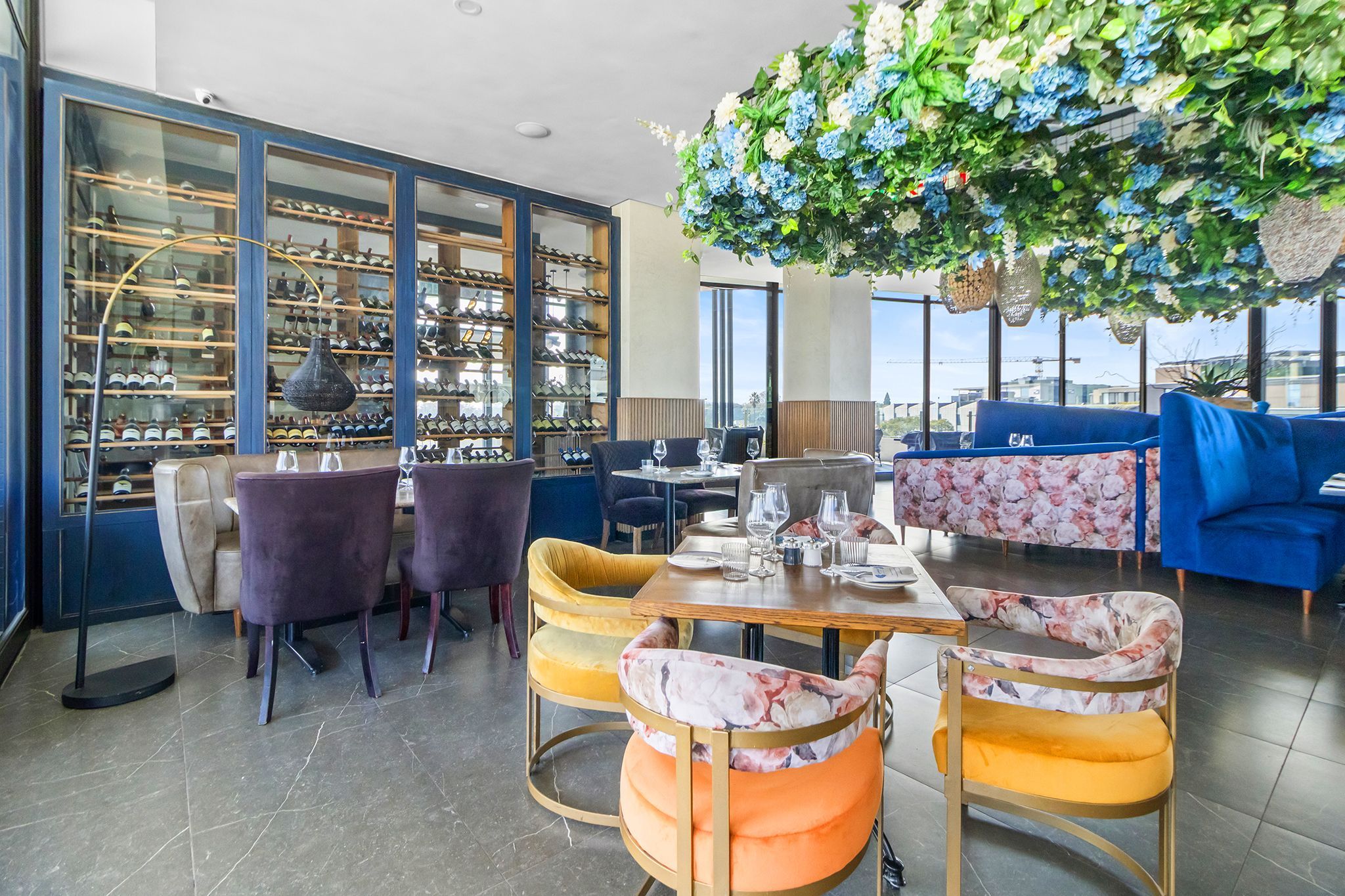 Um restaurante com adega, mesas, cadeiras e um sofá azul.