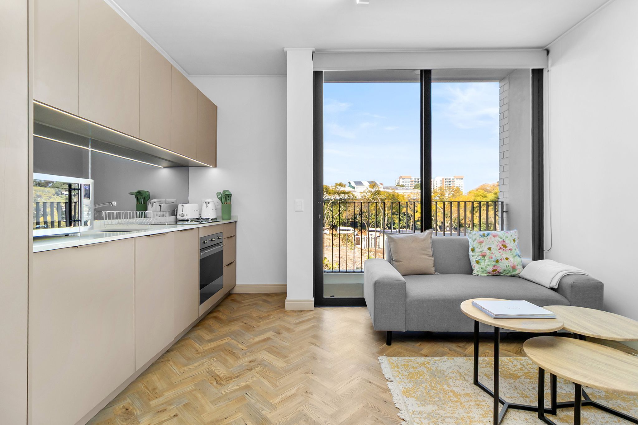 A modern apartment with a kitchen, a balcony with a view, and a seating area with a sofa and coffee table.
