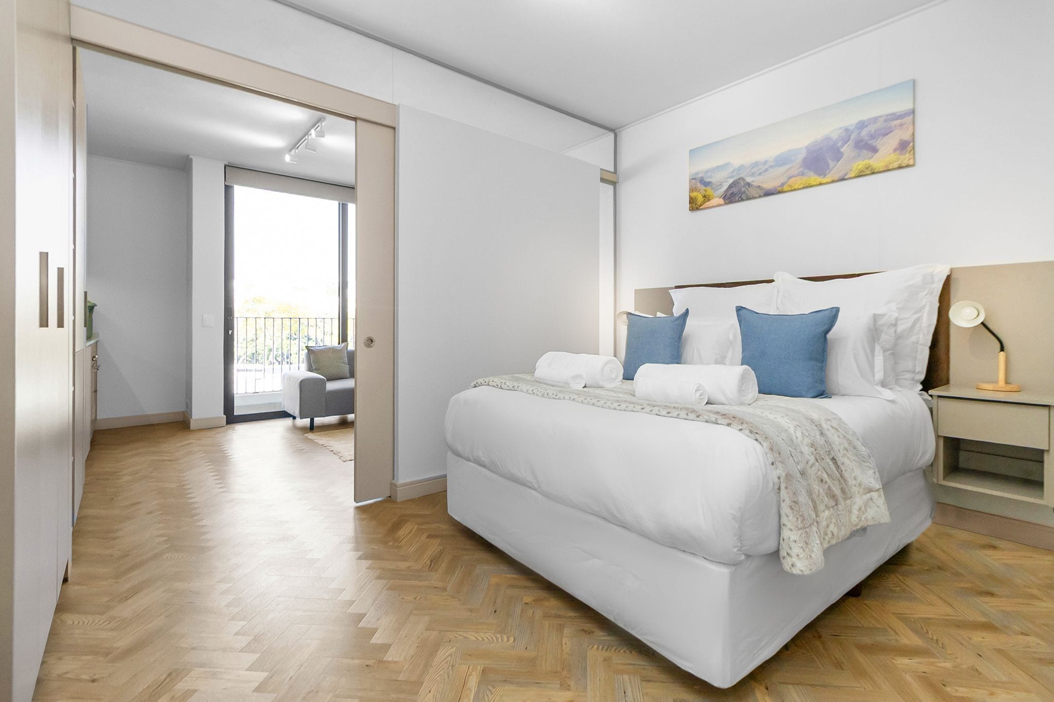 Une chambre à coucher moderne avec un grand lit, une table de chevet, une lampe et un tableau au mur.