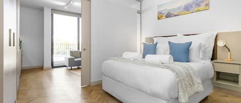 A modern bedroom with a large bed, a nightstand, a lamp, and a painting on the wall.