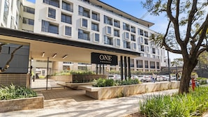 Ett modernt hotell med en framträdande skylt med texten ”ONE”, en överbyggd entré och en parkeringsplats med bilar.