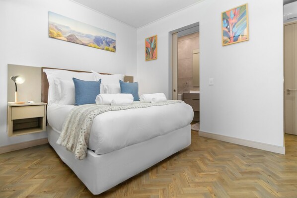 A modern hotel room with a large bed, a nightstand, a lamp, and two paintings on the wall. - One Rosebank 151 (Johannesburg)