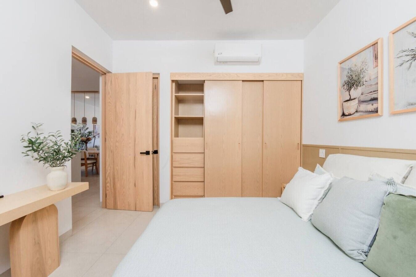 A bedroom with a bed, a bedside table, a wardrobe, and a potted plant.