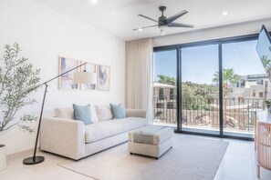 A modern living room with a sofa, ottoman, floor lamp, and artwork on the wall. - Coyote Tower 201 | Luxury Condo Walk to Marina (Cabo San Lucas)